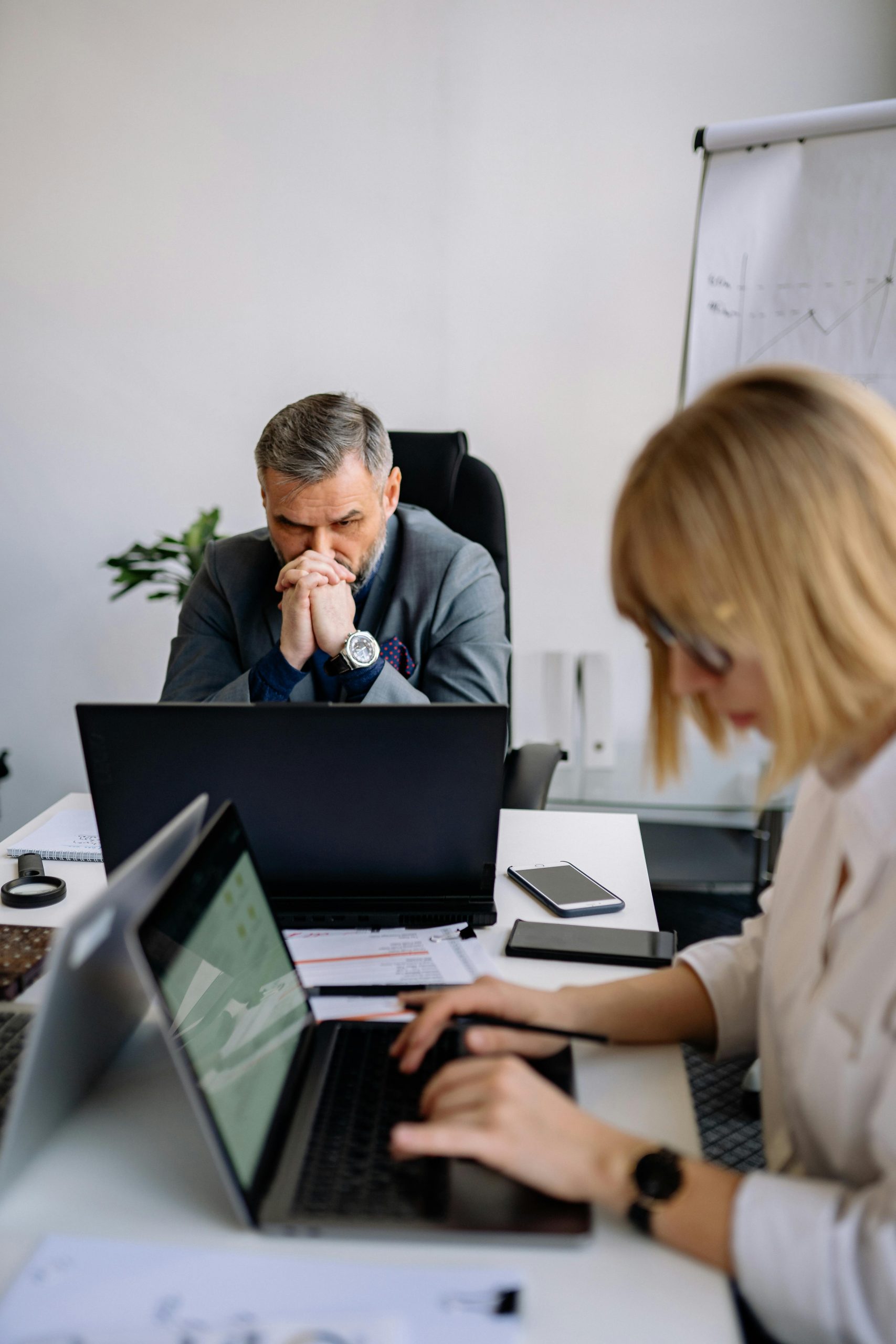 A stressed businessman and female colleague working intently on laptops in an office setting.